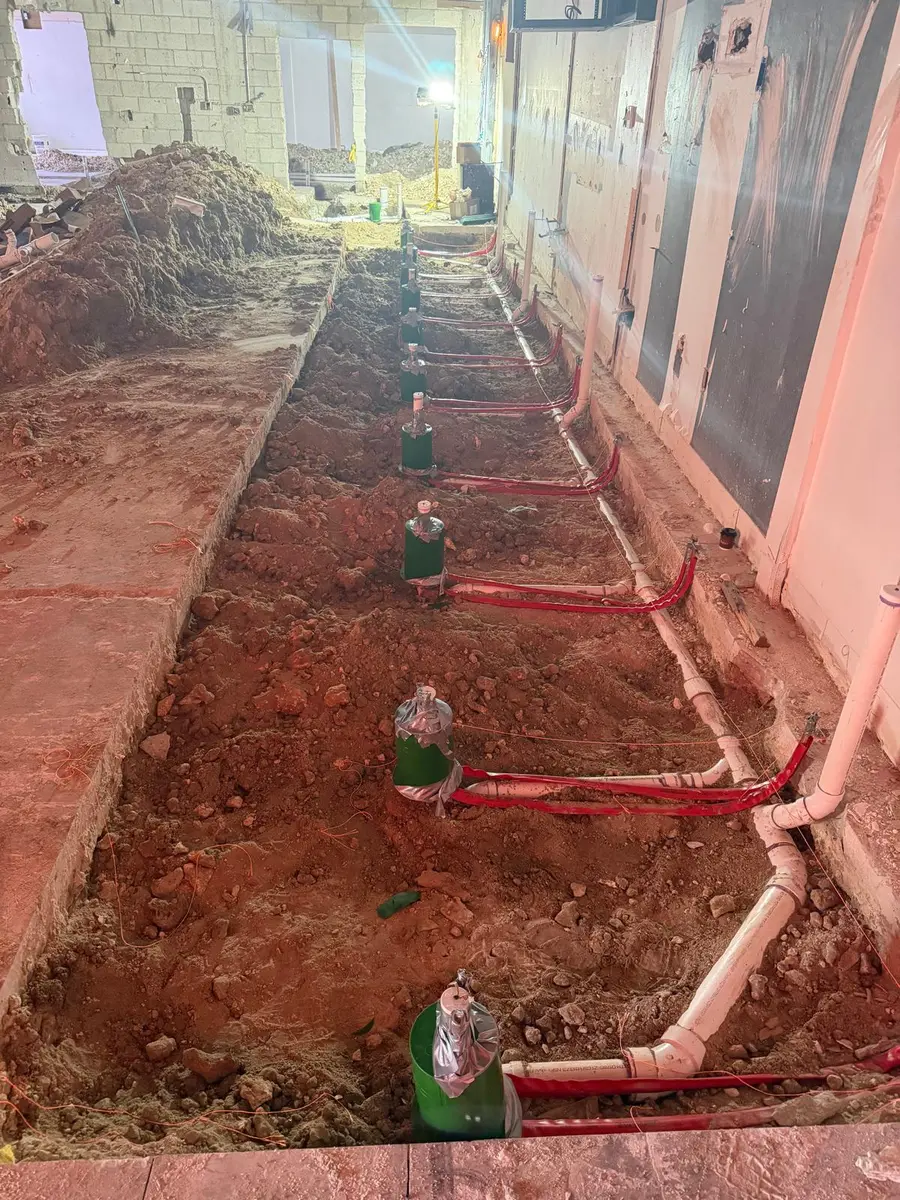Underground water and drain lines run in an open trench inside a building